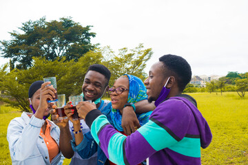 young black people standing in a park, giving a toast with drink in their glass cups