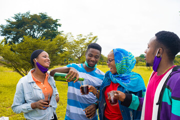 young black people standing in a park and pouring drinks into their glass cups