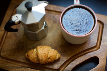 Aerial view of croissant, moka pot and glass of black coffee. Blurry and black background. 