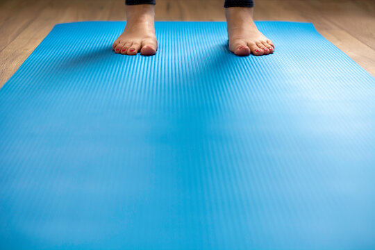 Woman standing on blue yoga mat. Feet with pink pedicure, low perspective. Concept of indoor workout, exercise