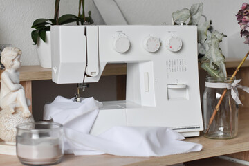 A fragment of a white electric sewing machine on a table in the scenery. Sews white cloth. Advertising sewing equipment. The controls of the sewing machine. Home crafts. Tailoring. Beautiful backgroun