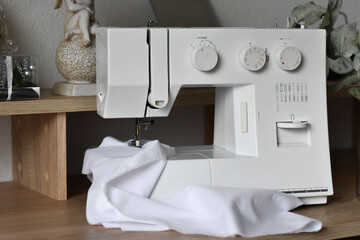 A fragment of a white electric sewing machine on a table in the scenery. Sews white cloth. Advertising sewing equipment. The controls of the sewing machine. Home crafts. Tailoring. Beautiful backgroun