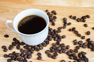 Black coffee placed on a wooden table with coffee beans.