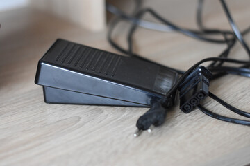 Black plastic control pedal for electric sewing machine. Electric plug. Advertising sewing...