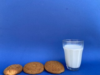 Glass of milk with brown oatmeal cookies on a blue background