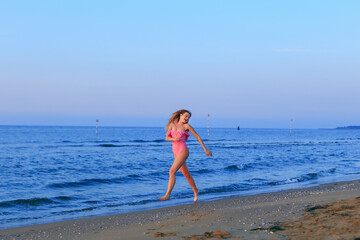 girl in a pink swimsuit run on a sand beach near the sea. the gi