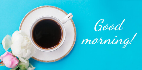 White cup of coffee,white and pink peonies and inscription GOOD MORNING! on a blue background.Summer romantic breakfast.Good morning concept.Selective focus, top view