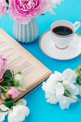 Summer romantic breakfast.White cup of coffee,open book and peonies on a blue background.Good morning concept.Selective focus with shallow depth of field