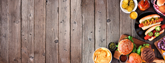 Summer BBQ food corner border with hot dog and hamburger buffet. Top view over a dark wood banner...