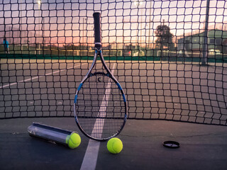 Tennis racket and tennis balls besides the net on outdoor tennis court.
