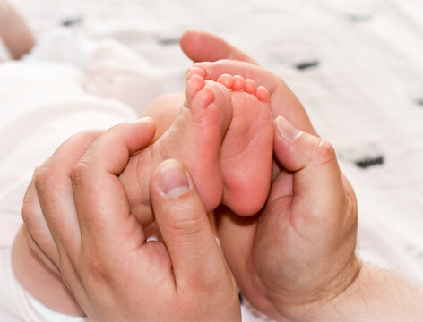 The father holds the baby's legs. Newborn in the hands of the Pope. Small children's feet, men's hands. Greeting card for father's day.