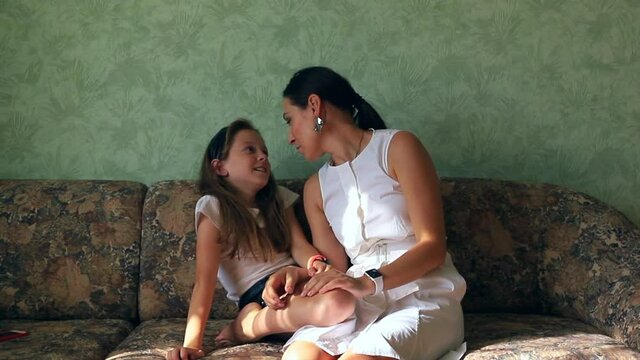 Mom and daughter fool around and have fun together on the couch in their apartment, emotionally gesticulating. High quality FullHD footage