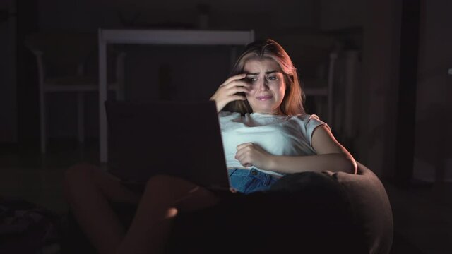 beautiful woman sitting on the couch while watching a horror movie TV at home in the evening. Scared girl watching tv on the living room. The concept of video games, entertainment, family, leisure