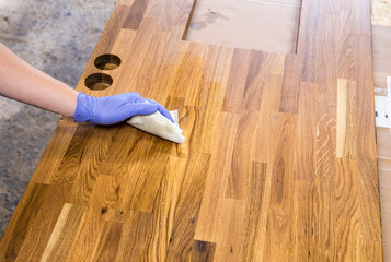 Person working, rubbing oiling with linseed oil natural wooden kitchen countertop before using....