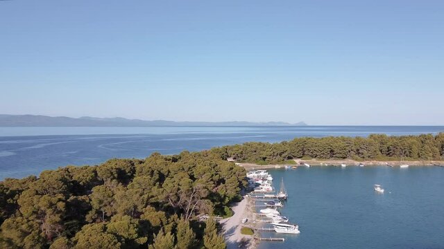 Drone flying above caique fishing boats, leading to calm sea. Aerial top view of Glarokavos lagoon at Kassandra Chalkidiki peninsula shoreline with green plantation.