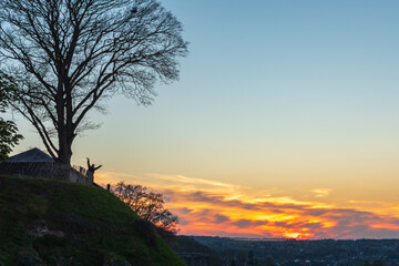 Man stretchs his arms on the top of a hill while watching the sunset over the city.