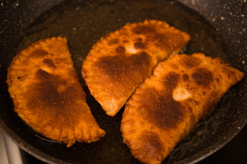 delicious fried pies with meat and greens cheburek in a pan with oil close-up