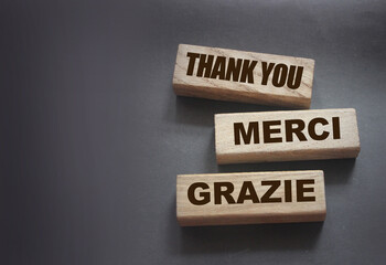 Text Thank you Merci Grazie on wooden blocks on black background. Gratitude expressed in English...