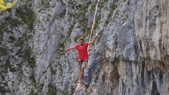 A man is walking along a stretched sling, Highline in the mountains, Man catches balance, Performance of a tightrope walker in nature, Highliner on the background of the mountains.