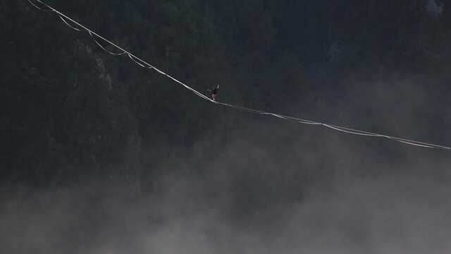 a man walks along a stretched sling high above the clouds. highliner catches the balance on a long and high sling pull in a canyon. Extreme sports in Bosnia and Herzagovina