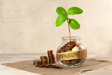 Pension. Glass jar with coins and a plant on the table and several coins nearby. The concept of finance and investment. 