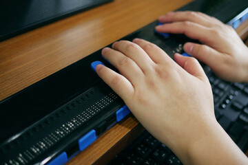 Close-up blind person woman hands using computer with braille display or braille terminal a...