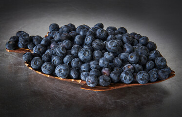 Wooden dish with fresh blueberries on a silver background, stylized