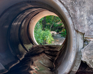 Fototapeta premium View of a small quiet river, with overgrown banks through the portal of the culvert