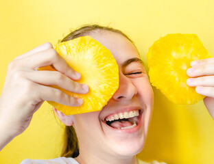 Portrait of teen girl smiling and laughing holding two round slices of pineapple before her face against yellow background. Summer food, summertime joy, vacation, holidays, minimal monochrome concept.