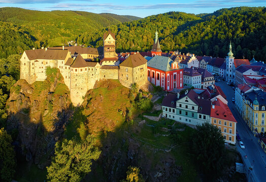 Aerial view of Loket Castle, Burg Elbogen, gothic style castle on rocky cliff, surrounded by green hills. Massive fortification illuminated by setting sun.  Karlovy Vary district, Czechia