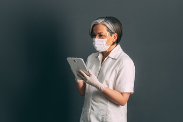 Experienced female doctor using tablet computer. Mature Caucasian woman in protective uniform working with digital gadget. Advanced technology in medicine concept Tinted image.