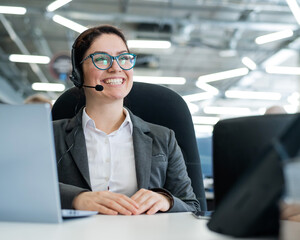 A happy female support operator is sitting at a desk and answering calls. Beautiful smiling woman...