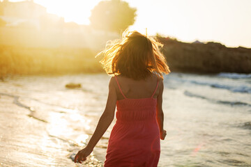 Back view of beautiful woman walking along beach and sea sunset background, hair blows in the wind....