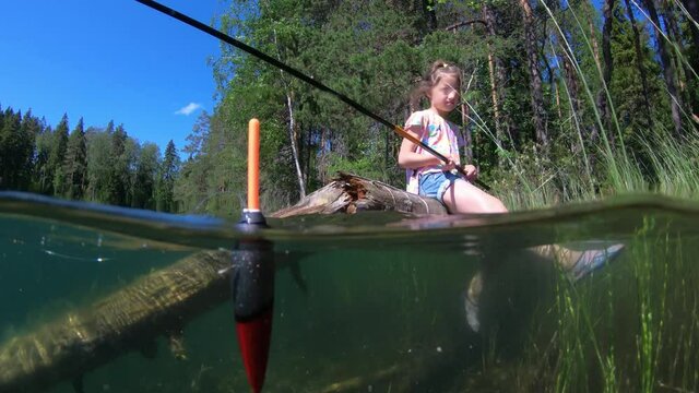 Little girl fishing on a green forest lake's coast with underwater view of fishing float and weed on a bottom
