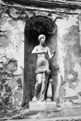 Black and white photo showing a marble statue of a beautiful naked young girl standing in a old building niche