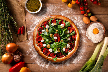 Brazilian pizza with dried tomato, arugula and mustard. Top view on wood background, close up....