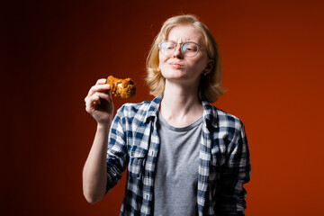 The blonde girl grimaces with displeasure and looks suspiciously at a chicken leg from fast food....