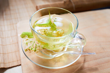 Transparent glass cup of herbal tea with linden flowers on a wooden background