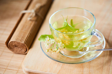 Transparent glass cup of herbal tea with linden flowers on a wooden background