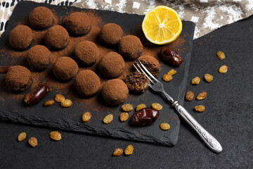Homemade vegan truffles with dried fruits, walnuts and raw cocoa powder served on black slate plate.