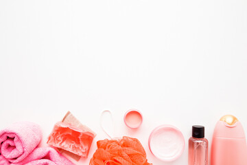Cream jars, shower bottle, essential oil, pink towel, orange wisp and soap on white table background. Relax products for body washing. Empty place for text or logo. Top down view.