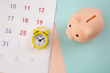 Savings concept. Piggy bank and alarm clock with calendar on colorful background.