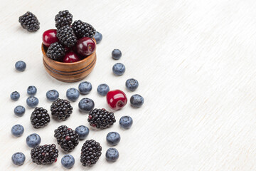 Berries in wooden box and on table: blackberry, cherry, blueberry and raspberry.
