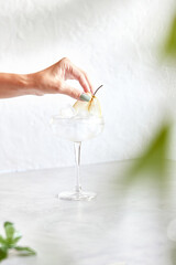 Classic martini with ice. Female hand decorates cocktail with pear slice. On a light background