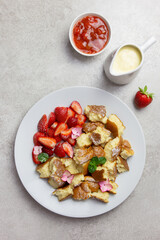 Kaiserschmarren or Kaiserschmarrn, traditional Austrian or German sweet pancake dessert, with berry, strawberry jam or rote grutze and vanilla pudding sauce. Top view.