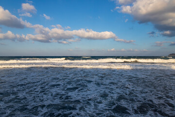 Obraz premium Beautiful black beach with coast and sea in Vlichada with blue sky background with white clouds and sea.