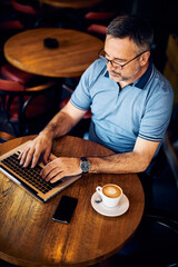 Mature adult man sitting in coffee shop and using laptop for online dating.