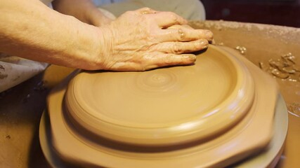 Close up of male potter throwing clay for plate onto pottery wheel in ceramics studio - shot in slow motion
