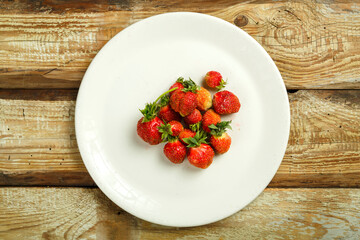 Fresh ripe strawberry on a white plate on a wooden table.