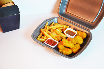 Yummy French fries, chicken Nuggets, sauce, paper bag, white background. Binge eating. food delivery